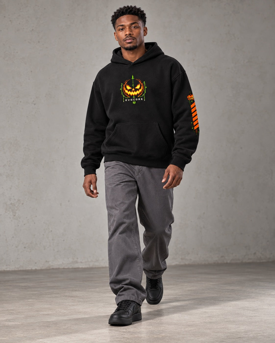 AI model visualization of the black EvoCore Pumpkin Mecha hoodie in a walking pose, showing the orange and lime chest emblem and left-sleeve print.