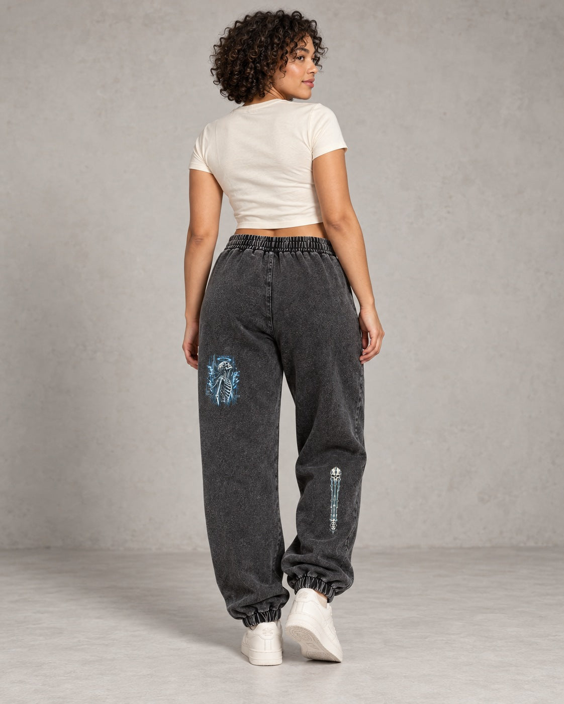 AI model visualization of snow-washed black EvoCore Bone Circuit joggers from behind, showing separate skeleton graphics on the left rear thigh and right calf.