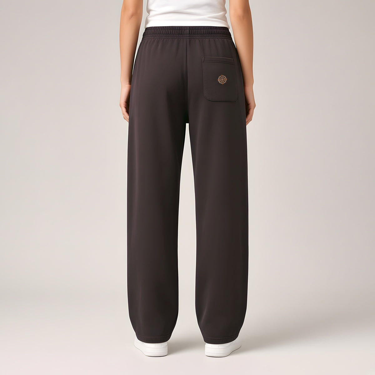 Back view of the Dark Purple EvoCore Afterlife FM Golden Static Loose Sweatpants showing the back-pocket emblem, warm light-grey studio.
