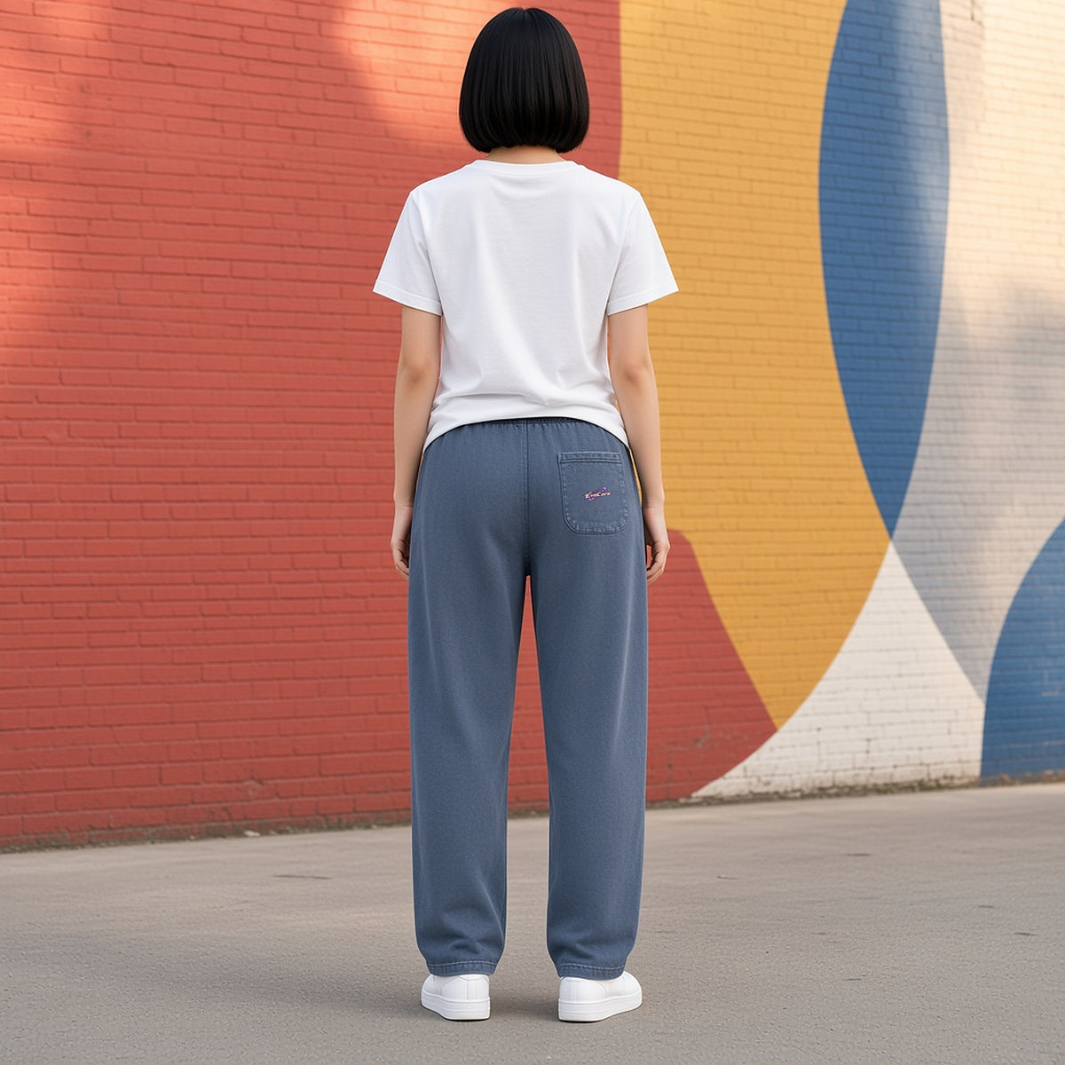 Back view of EvoCore Ghost Cache Navy Blue loose sweatpants in front of a painted brick mural wall, orbit logo on the rear patch pocket.