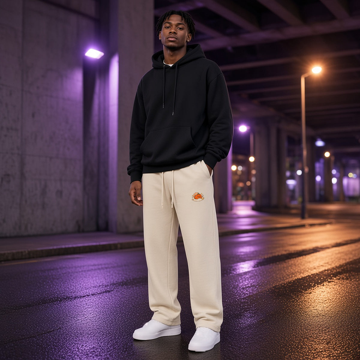 Front view of EvoCore Pumpkin Pause Washed Sweatpants in Apricot worn under a city overpass at night, sleepy pumpkin print at the thigh.