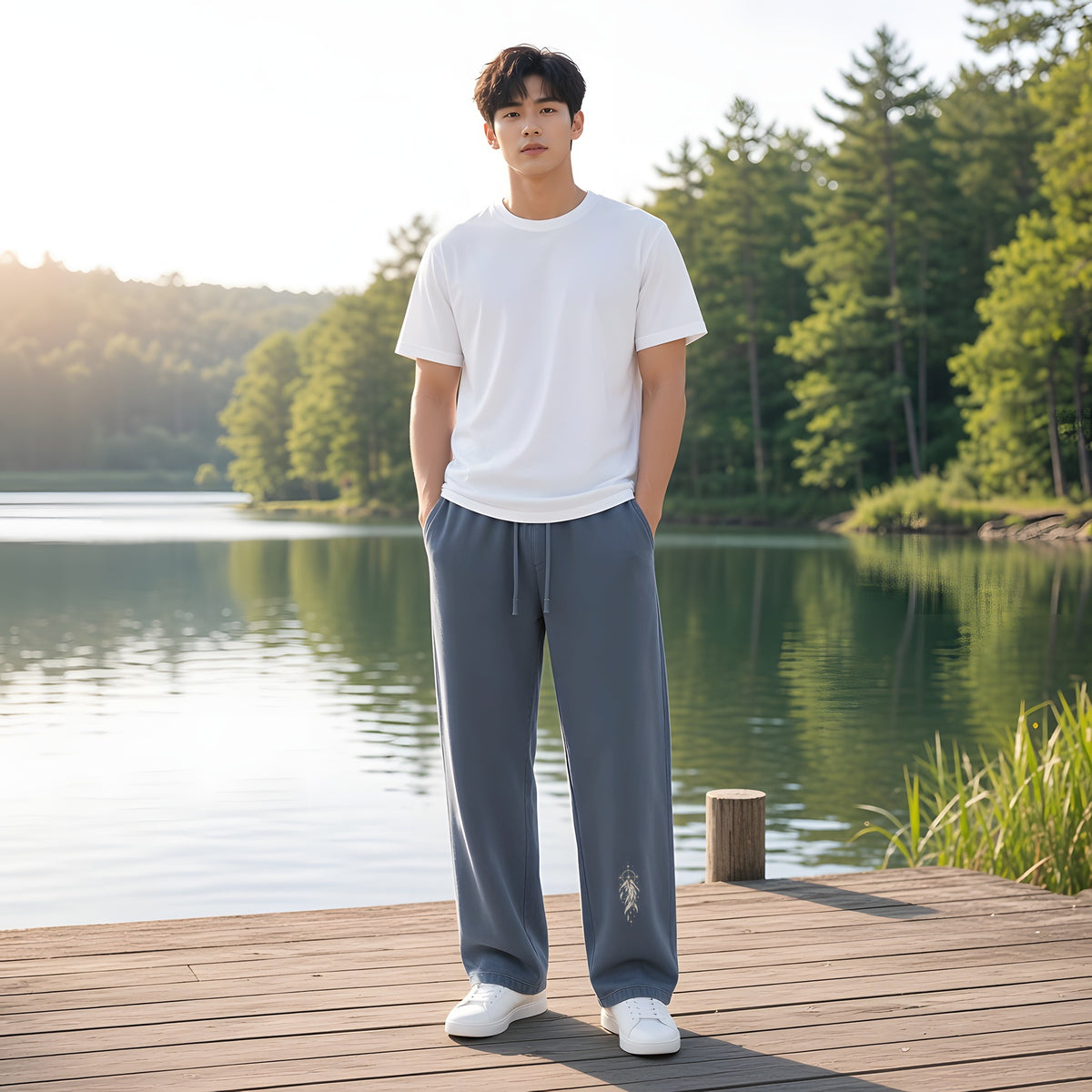 Model wearing the Navy Blue EvoCore Seraph Bluehour Loose Sweatpants, front view showing the leg print, lakeside wooden pier, sunny.