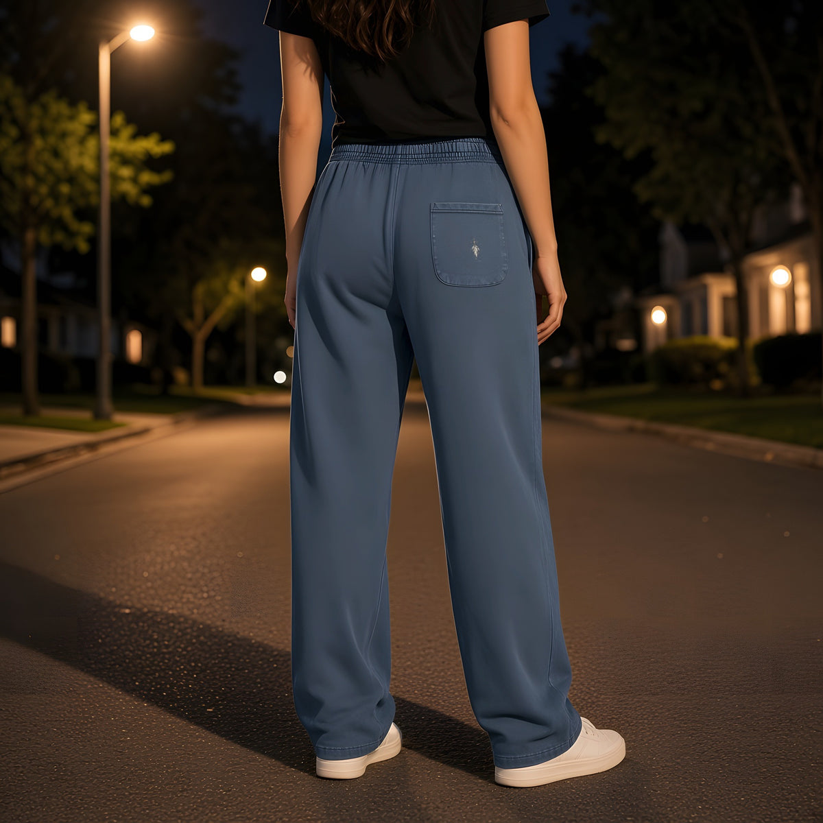 Back view of the Navy Blue EvoCore Seraph Bluehour Loose Sweatpants showing the back-pocket emblem, night street under a streetlamp.