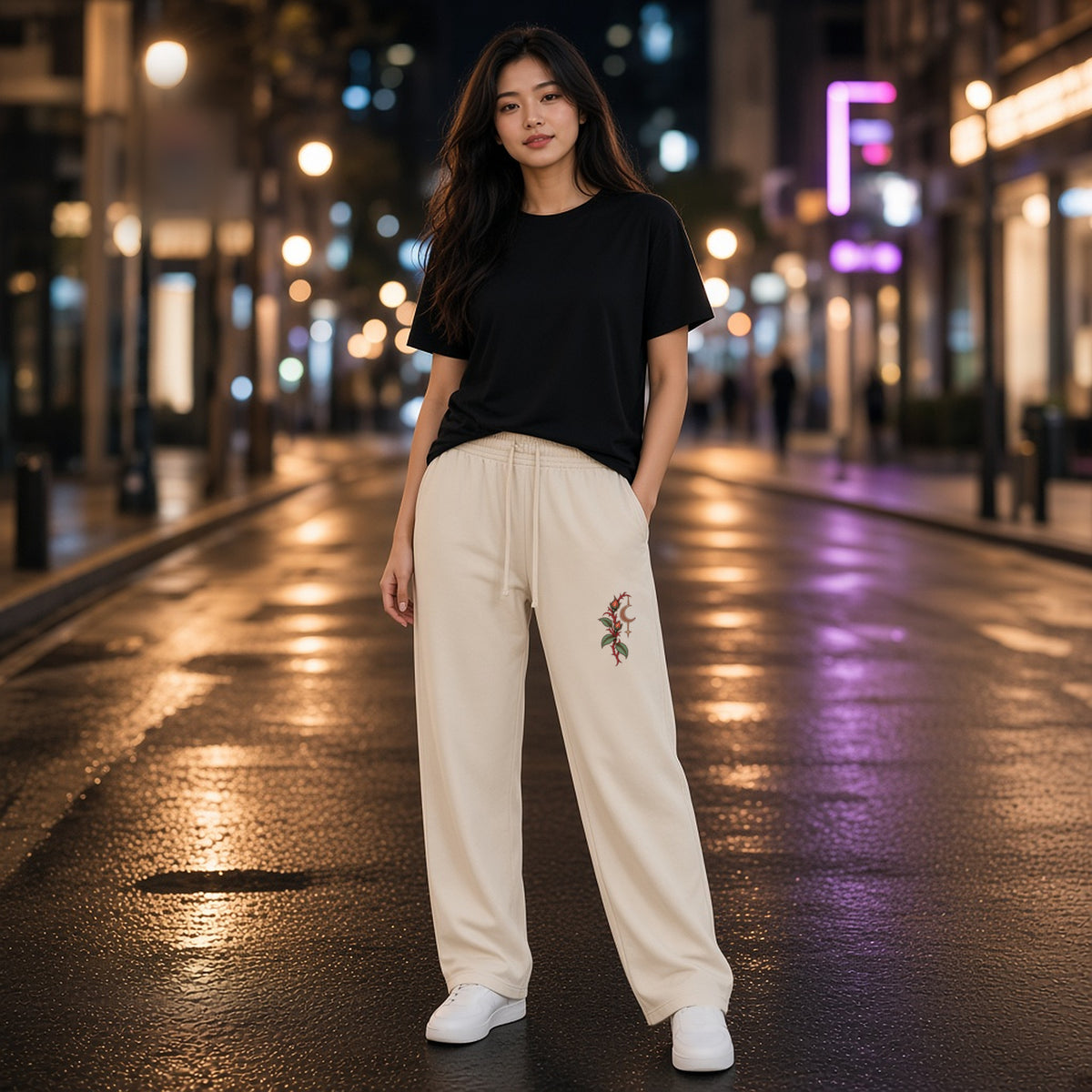 Front view of EvoCore Thornlight Conservatory Apricot loose sweatpants worn on a lamp-lit street at night, thorned stem and crescent print on the left leg.