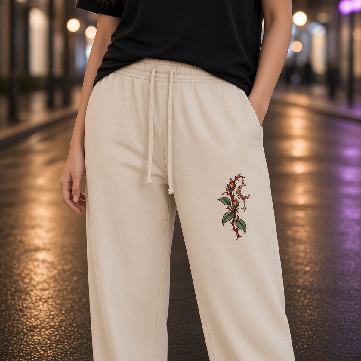 Close-up of the red thorned stems, green leaves and crescent print on the left leg of EvoCore Thornlight Conservatory Apricot sweatpants.